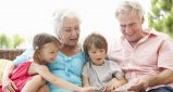 Grandparents And Grandchildren Reading Book On Garden Seat